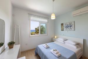 a white bedroom with a bed and a window at Protaras Sunrise Zen Seafront Villa in Protaras