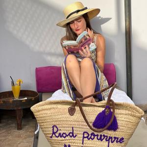 a woman in a straw hat sitting in a chair reading a book at Riad Pourpre Medina in Marrakesh