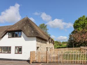 a white house with a thatched roof and a wooden fence at Rose Cottage at Treaslake Farm in Honiton