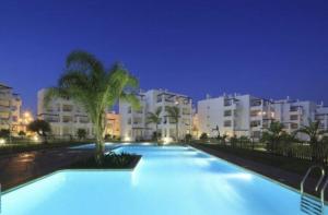 a swimming pool in front of some buildings at night at 2-Bed Penthouse Apartment in Roldán