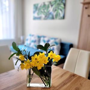 Silver Lodge Apartment 1 Eger في إغير: إناء من الزهور الصفراء على طاولة خشبية