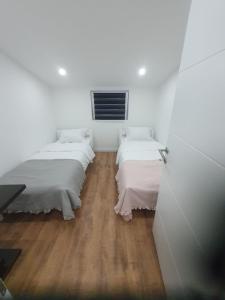 two beds in a room with white walls and wood floors at MB Apartman in Čapljina
