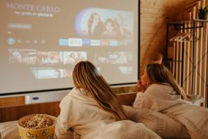 dos mujeres sentadas en un sofá frente a una pantalla en Welmoon Villas Paisaje, en Caravaca de la Cruz