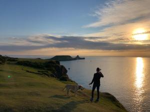 a woman and a dog standing on a cliff near the water at Ger Tŷ in Swansea