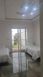 Dieses weiße Zimmer verfügt über 2 Betten und ein großes Fenster. in der Unterkunft bel appartement de vacances in Saidia 