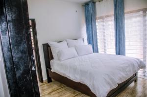 a bedroom with a bed with white sheets and blue curtains at Nsunge Nsunge Farm and Natural Resort in Lusaka
