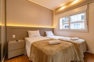 twee bedden in een kleine kamer met een raam bij Rosa Edifício Reservas das Orquídeas in Gramado