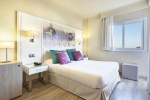 a bedroom with a large bed with purple and green pillows at Grupotel Maritimo in Port d'Alcudia