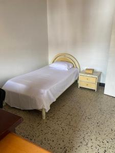 ein Schlafzimmer mit einem Bett und einem Nachttisch mit einer weißen Tagesdecke in der Unterkunft CASA FAMILIAR AMPLIA MUY FRESCA in Medellín