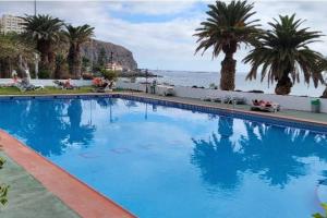 a large swimming pool with palm trees and the ocean at Comodoro Los Cristianos 601T in Los Cristianos