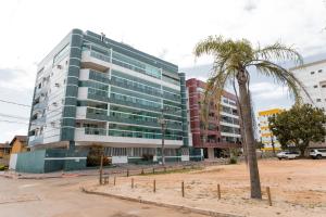 瓜拉帕里的住宿－2 Qtos 1 Suíte com Ar condicionado, Varanda, 50 m da Praia da Bacutia，一座高大的建筑,前面有一棵棕榈树
