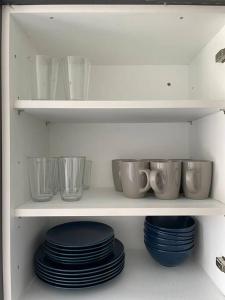 a white shelf with plates and cups and bowls at Grays Serviced Apartment in Stifford