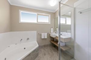 Baño blanco con bañera y lavamanos en Ramada Resort by Wyndham Phillip Island, en Cowes