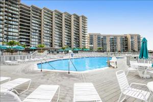 a swimming pool with white chairs and a large building at Sea Colony --- 38924 Cypress Lake Circle Unit 56079 in Bethany Beach