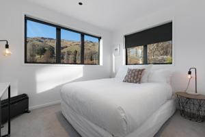 a white bedroom with a large bed and two windows at Cardrona Vista Apartment in Cardrona