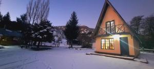 una pequeña casa en la nieve con las luces encendidas en Cabañas Rio Hermoso en Cerro Negro