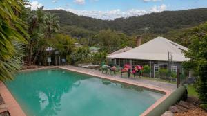 a swimming pool with two chairs in front of a house at Lilly Pilly Arthouse in Stanwell Park