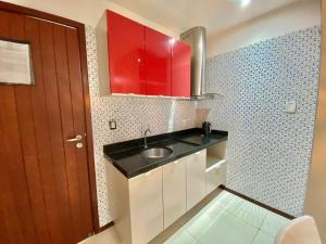 una pequeña cocina con fregadero y armarios rojos en Bangalô Villas do Pratagy 1 Dormitório e Varanda, en Maceió