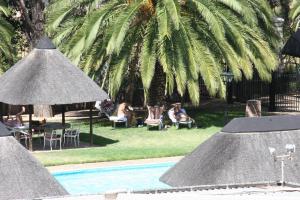 a swimming pool with people sitting in chairs and a palm tree at Mercure Hotel Windhoek in Windhoek