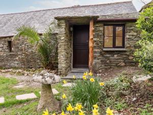 a stone cottage with a black door and flowers at Downrow Barn in Tintagel