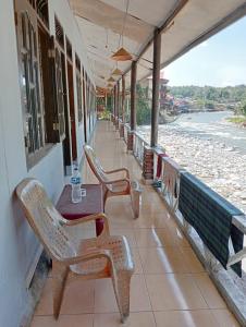 a porch with chairs and a table and a view of the water at Sumatra Jungle Trek In & Orangutan Trips in Bukit Lawang