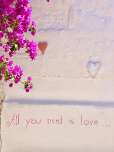 a white wall with purple flowers and a sign that reads all you need is love at Masseria Rienzo in Ostuni