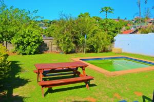 eine Holzbank in einem Hof mit einem Pool in der Unterkunft Seas of Ships Guest House in Durban