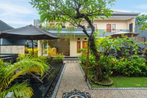 a garden with chairs and an umbrella in front of a house at Liliy Guest House Kuta - Badung in Legian