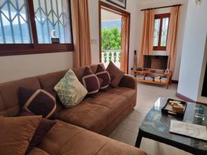 ein Wohnzimmer mit einem braunen Sofa und einem Glastisch in der Unterkunft The Drake Seaside Apartment in Bel Ombre