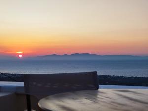 - un coucher de soleil sur l'océan avec une table et une chaise dans l'établissement Panorama Oia Apartments, à Oia