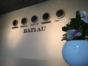 un mur avec des horloges, un vase et des fleurs dans l'établissement Baitau Hotel Aktobe, à Aqtöbe