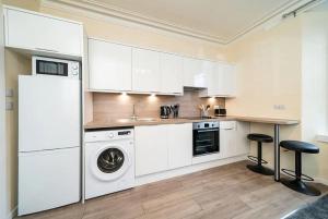 cocina con armarios blancos, lavadora y secadora en Rosemount Residence - SJA Stays en Aberdeen