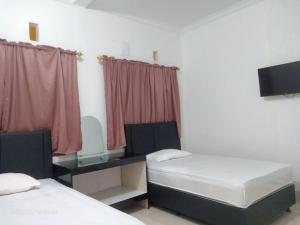 a room with two beds and a desk with a tv at Permata Homestay Kotamobagu Mitra RedDoorz in Poyowa-besar