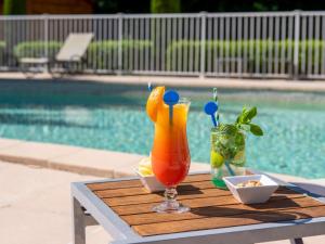 uma bebida sentada numa mesa ao lado de uma piscina em Novotel Aix-en-Provence Beaumanoir em Aix-en-Provence