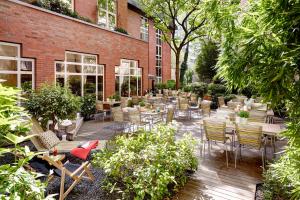 eine Terrasse mit Tischen und Stühlen vor einem Backsteingebäude in der Unterkunft Lindner Hotel Cologne City Plaza, part of JdV by Hyatt in Köln