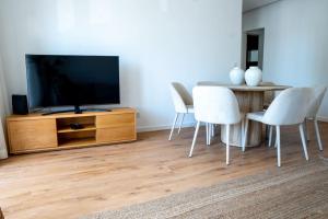 uma sala de estar com uma televisão e uma mesa com cadeiras brancas em NEW Estrela da Praceta Apt w/ 3 Suites & Oceanview em Carcavelos