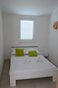 Cama blanca con almohadas verdes y ventana en Villa Vinko, en Trogir