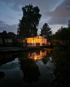 une maison éclairée la nuit à côté d'une masse d'eau dans l'établissement Rustig gelegen chalet Solvo met terras aan het water, à Geel