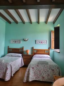 two beds in a bedroom with blue walls and wooden floors at Posada los Taranos in Valdaliga 