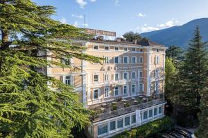 un grand bâtiment blanc avec des arbres devant lui dans l'établissement Hotel Adria, à Merano
