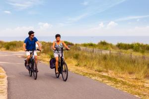 two people riding bikes down a road near the ocean at Dormio Resort Nieuwvliet-Bad in Nieuwvliet