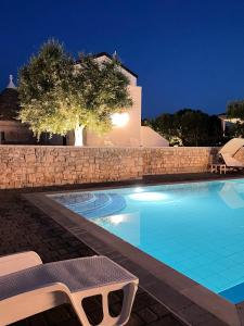 - une piscine avec un mur en pierre et un arbre la nuit dans l'établissement Trullisia Bed and Breakfast, à Alberobello