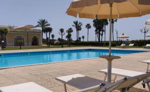 a chair with an umbrella next to a swimming pool at Parco dei Principi Hotel in Roccella Ionica