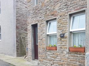 um edifício de tijolos com duas janelas com flores em 1 Taits Flat em Orkney