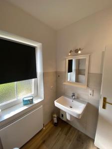 ein weißes Bad mit einem Waschbecken und einem Fenster in der Unterkunft Wulfen Auszeit & Meer Wulfen in Westfehmarn