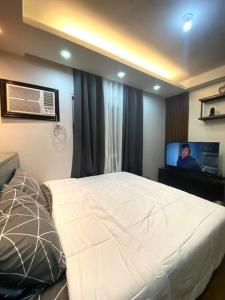 um quarto com uma cama branca e uma televisão em At the Heart of Davao w/ Wifi, Netflix & Disney+ em Dávao