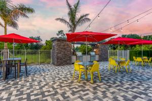 un patio avec des tables, des chaises et des parasols rouges dans l'établissement Home2 Suites By Hilton Vero Beach I-95, à West Vero Corridor