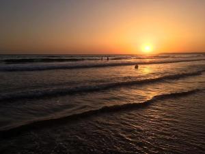 una puesta de sol en la playa con gente en el agua en Apartamento Conil, en Conil de la Frontera