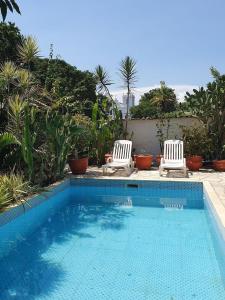 una piscina con 2 sillas blancas al lado en Andorinhas "Mini casa de hóspede" en Niterói