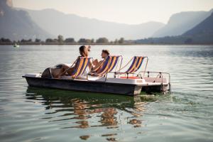 Parc Hotel Am See في كالدورا: يجلس شخصان على كراسي على قارب في الماء